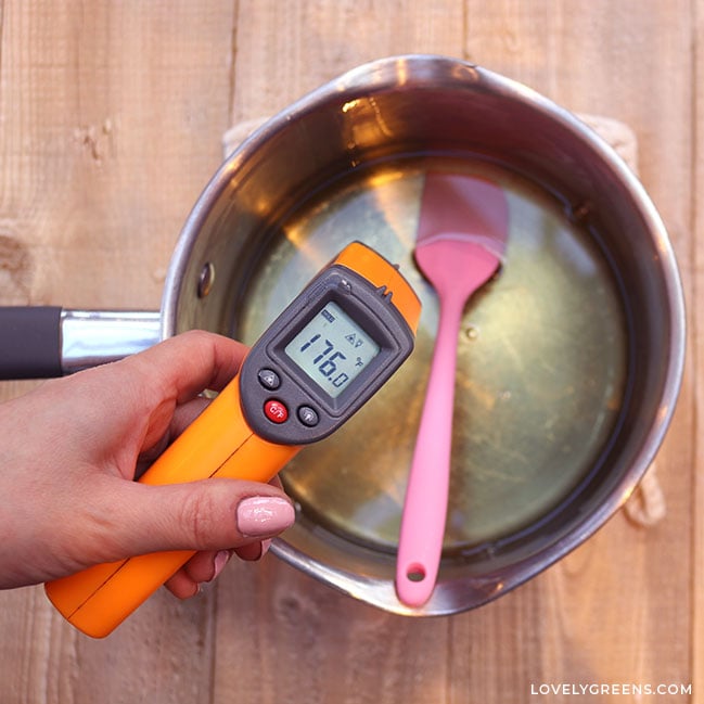 A hand holds an infrared temperature-gun over a pan of wax. It says the melted wax is 176 degrees F.