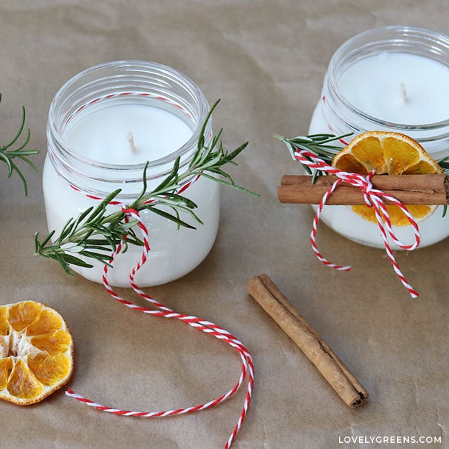 One candle is already decorated with red and white bakers twine holding a sprig of rosemary, a dried orange slice, and a cinnamon stick. Another is one is being started.