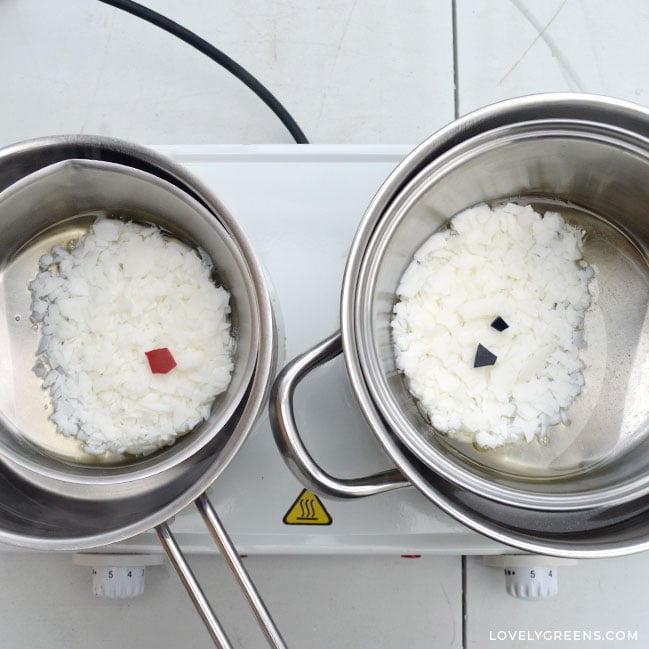 Two pots of wax are melting in double boilers. Each contains a small colored chip on top of white soy wax.