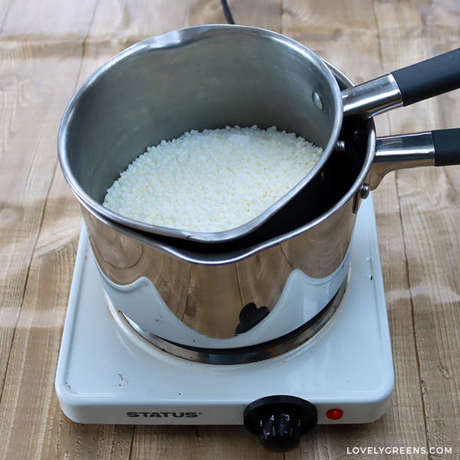 Two stainless steel pans sit nested inside one another on a hot plate. The inner pan contains white wax pellets.