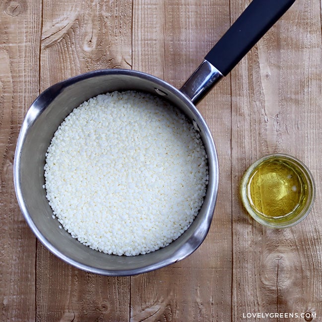 Looking down at a saucepan with spouts filled with white wax beads. To the right is a small glass ramekin filled with yellow liquid - the fragrance oil.