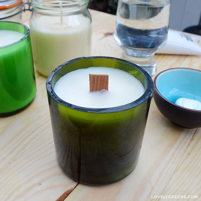 A close-up of a candle made using a thick-glass green wine bottle. It's been cut and then filled with white wax and a wooden wick.