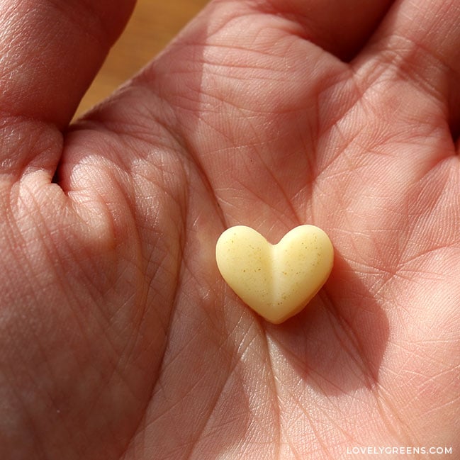 Close-up of a heart-shaped lotion dot in the palm of a hand. It's a light yellow color with tiny light brown flecks on top.