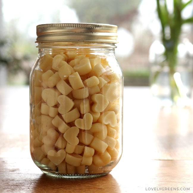 A pint-sized mason jar filled with heart-shaped lotion dots sits on a wooden table top.