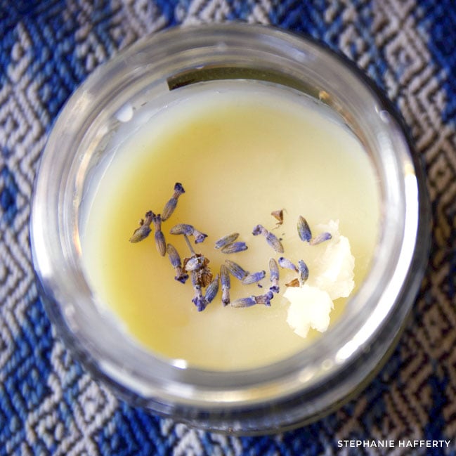 Looking down at a small round glass vessel filled with a creamy salve. Lavender buds are sprinkled on top.