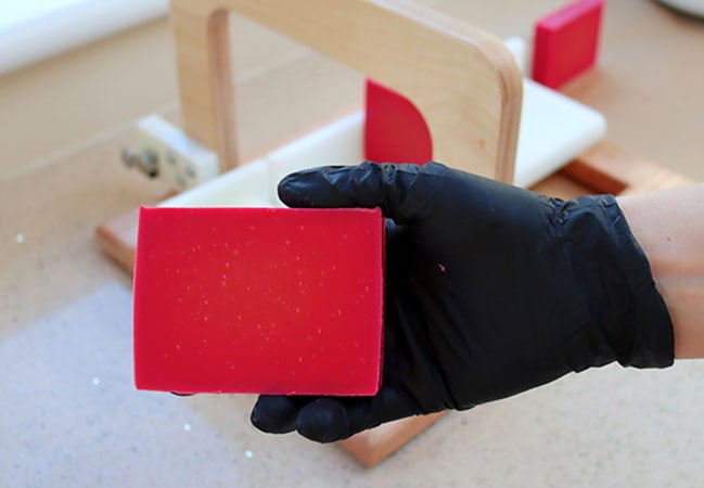 A gloved hand holds a freshly cut bar of deep red Himalayan rhubarb soap.