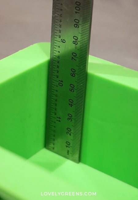 A metal ruler measuring the depth of a green soap mold.