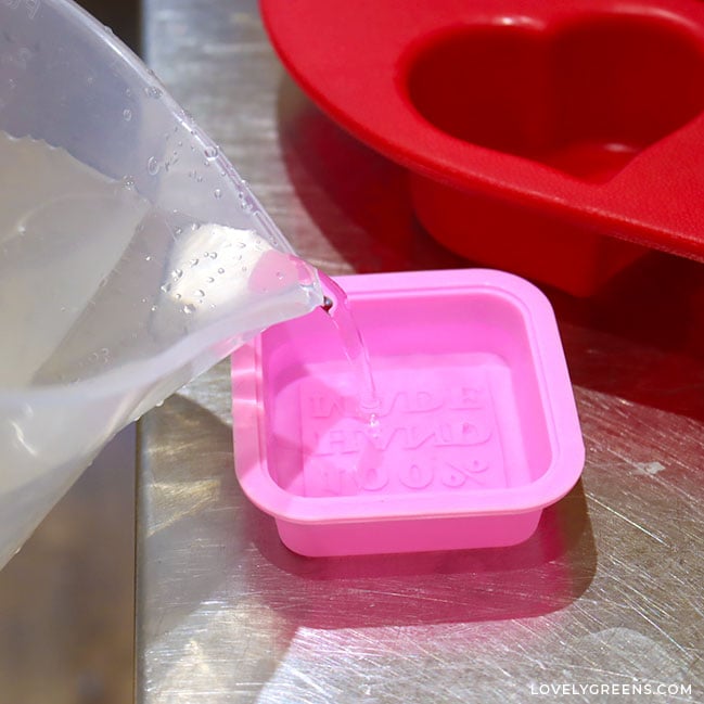 A clear jug pours water into a small pink soap mold.